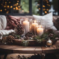 candles and pine cones on a table in front of a couch with christmas lights behind them