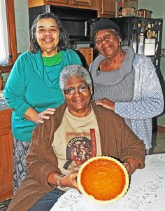 three women standing around a table with a pie on it