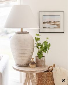 a white lamp sitting on top of a table next to a basket filled with plants