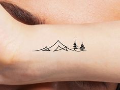 a person with a tattoo on their arm that has mountains and trees in the background