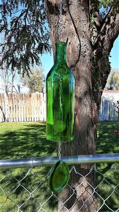 a green glass bottle hanging from a chain link fence next to a tree in the yard