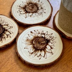 three wooden coasters with sunflower designs on them sitting on a table next to a cup