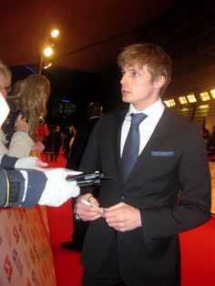 a man in a suit and tie is shaking hands with someone on the red carpet