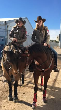 two women in cowboy hats riding horses on dirt road next to building and fenced area