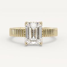 a yellow gold ring with an emerald cut diamond in the center and thin band around it