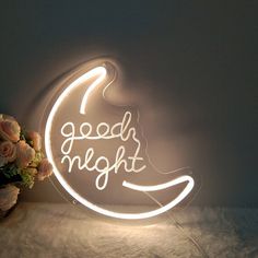 a neon sign that says good night on the side of a wall next to a vase with flowers