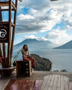 a woman sitting on top of a wooden bench next to a large body of water