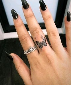 a woman's hand with a butterfly tattoo on her left ring and black nail polish