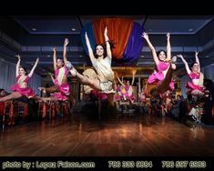 a group of women in pink and gold outfits dancing on a wooden floor with their hands up