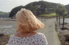 the back of a woman's head as she walks down a path near water