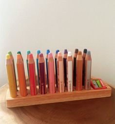 there are many different colored crayons in this wooden holder on the table,