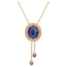 Enchanting tanzanite necklace from our Starlight Collection. -Handmade of 18K rose gold. -Center Stone: deep purplish blue cabochon cut tanzanite, 73,21ct. -Handset with 332 rose-colored sapphires, ca 10ct total. -2 dangling cabochon cut tanzanites, 8ct total -The length of the necklace and dangling tanzanites is adjustable by pressing the button in the back and pulling on either. Imagine hot, liquid magma rising from the depths and slowly cooling. Only a few million years later, after some tric Tanzanite Pendant Design, Blue Sapphire Pendant Designs, Luxury Gold Tanzanite Necklaces, Elegant Tanzanite Round Pendant Necklaces, Gold Tanzanite Pendant Jewelry, Luxury Tanzanite Pendant Jewelry, Luxury Tanzanite Pendant Necklace, Colored Sapphires, Tanzanite Pendant