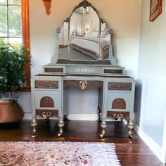 an antique desk with a mirror on it in front of a rug and potted plant