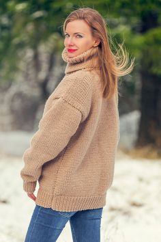 a woman standing in the snow wearing a sweater and jeans