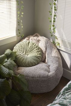 a round chair with a green pillow on it next to a potted plant and window