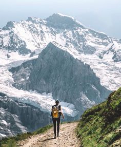 a man with a backpack walking up a trail towards a mountain range covered in snow