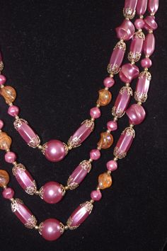 "Vintage 3 Strand Beaded Necklace: Purple Pearls & Orange Beads w/ Gold Filigree Beads, 1960s Unusual three-strand necklace with various-shaped purple pearls with gold filigree endcaps, as well as clear orange plastic beads with a slight aurora borealis sheen. A gorgeous mid-century masterpiece! Hook clasp, marked \"Hong Kong.\" The shortest strand is 20\" long, but with the expander is is 22.5\" long." Vintage Beaded Necklaces With Colorful Beads, Vintage Beaded Chain Necklaces, Vintage Beaded Party Necklace, Vintage Beaded Necklaces For Party, Retro Party Beaded Necklaces, Large Vintage Beads For Jewelry Making, Vintage Gold Beaded Necklaces With Colorful Beads, Vintage Party Beaded Necklaces With Large Beads, Vintage Beaded Necklace With Round Beads For Party