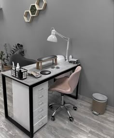 a desk with a chair, lamp and other items on it in front of a gray wall