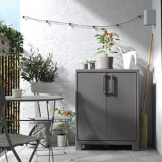 an outdoor patio with potted plants on the table and chairs, next to a gray cabinet