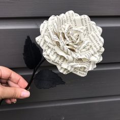 a person is holding a fake flower made out of book pages and black leaves on the side of a building