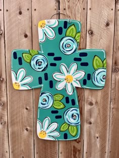 a blue and white flowered cross hanging on a wooden fence