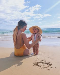 a woman sitting on top of a sandy beach next to a baby in a yellow bathing suit