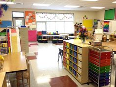 an empty classroom with lots of desks and colorful books on the shelves in it