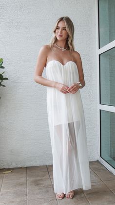 a woman in a white dress standing on a tile floor next to a wall and window