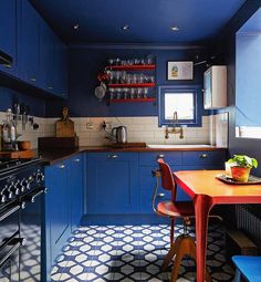 a kitchen with blue cabinets and an orange table in front of a stove top oven