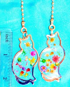 Set of Two - Kitty Cat Flowers Floral Metal ~ Ceiling Fan/Light Pull Chains This ceiling fan pull makes a great gift for the special person in your life.  This set includes two cat silhouette with white & purple flowers embedded inside the fan pulls with an aluminum foil background.  The design includes little bubbles in that give it even more charm.  It measures about 2" long and 1" wide.  It is made of metal and is beautifully decorated. The pull chain comes with its own ball and chain with al Metal Ceiling Fan, Ceiling Fan Light Pulls, Foil Background, Ceiling Fan Pulls, Ceiling Fan Light, Fan Pulls, Cat Flowers, Light Pull, Metal Ceiling