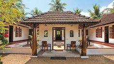 a white house with red trim and wooden doors on the front door is surrounded by palm trees