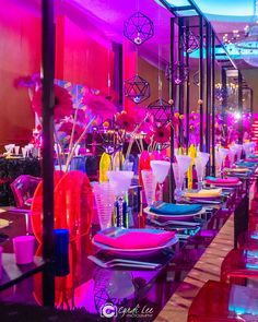 a long table with many different colored plates and glasses on it, all in front of a purple light