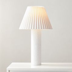 a white lamp sitting on top of a table next to a light fixture with a pleated shade