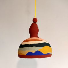 a multicolored lamp hanging from a yellow cord on a white wall with mountains in the background