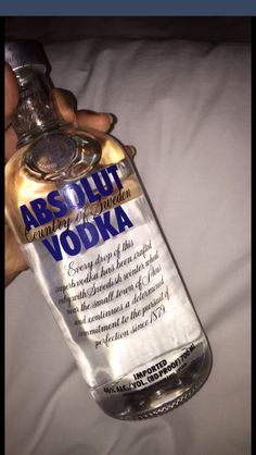 a person holding a bottle of vodka on top of a white bed sheet with the label abs ult vodka