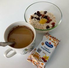 a cup of coffee, cereal and milk on a white counter top next to a bag of granola