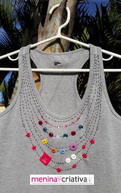 a gray tank top with multi colored buttons and chains hanging on a clothes rack in front of palm trees