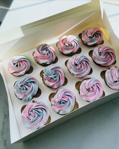 twelve cupcakes with pink and blue frosting in a white box on a table