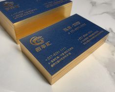 two blue and gold business cards sitting on top of a white countertop next to each other