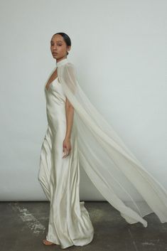 a woman in a white dress with a long veil on her head is standing against a wall