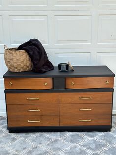 a wooden dresser with two drawers and a basket on top, in front of a garage door