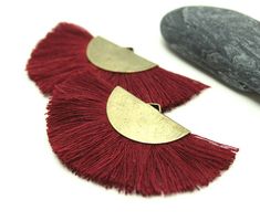 two pairs of red tasseled earrings on top of a white table next to a rock