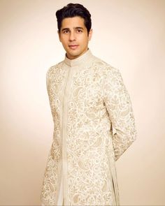 a man in a white and gold sherwa with his hands on his hips