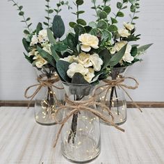 two clear vases with white flowers and greenery