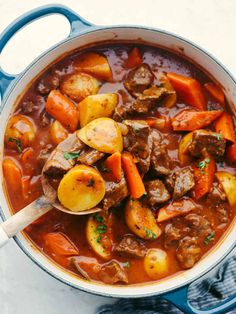 a pot full of stew with carrots, potatoes and meat in it on a white surface