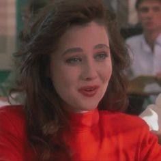 a woman with long brown hair wearing a red shirt and sitting in front of a man