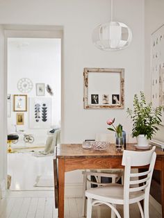 a dining room table with chairs and pictures on the wall above it, along with two vases filled with flowers