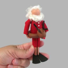 a hand holding a small toy with a red suit and white beard on it's head