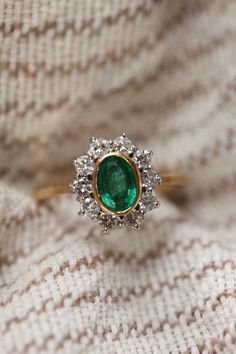 an emerald and diamond ring on top of a blanket