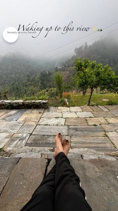 a person is laying down with their feet up in the air and foggy mountains behind them